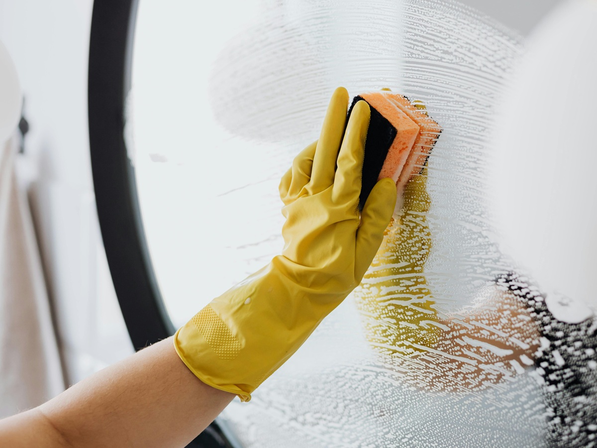 Hand wearing a rubber glove cleaning a mirror with a sponge – French chores vocabulary illustration.